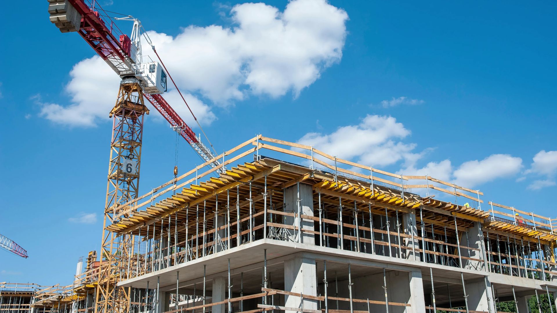Baustelle mit Betongebäude und rotem Baukran vor blauem Himmel mit Wolken